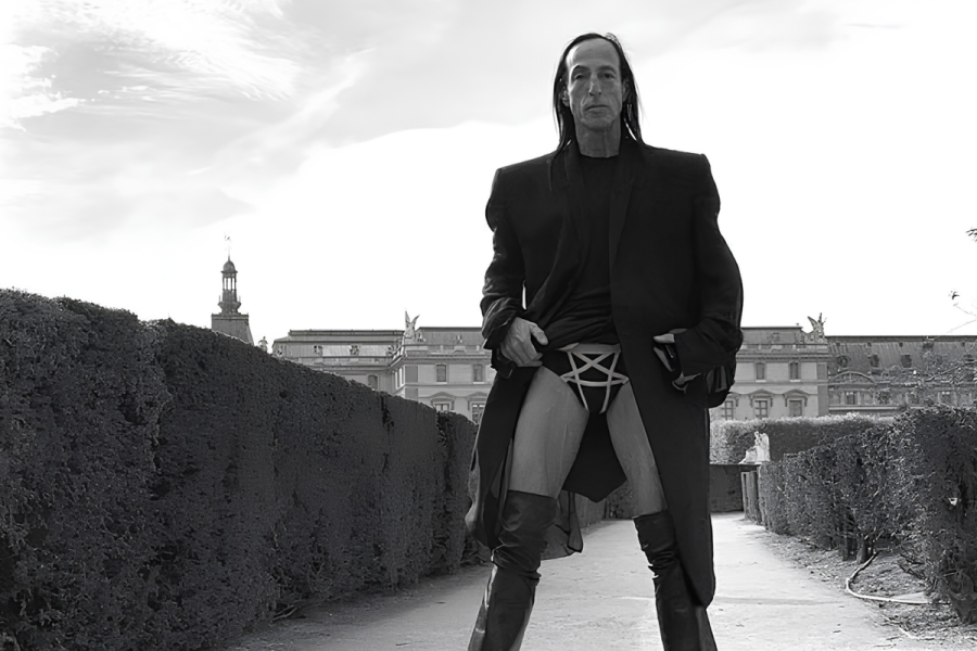 Rick Owens poses outdoors in a dark coat and thigh-high
