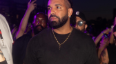 Drake in a black tee wearing gold accessories